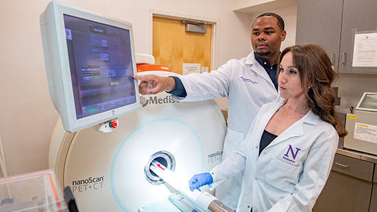 Two technicians use a scanner, one points at an attached screen